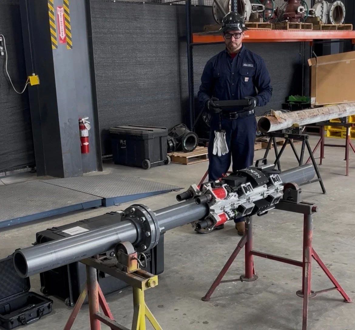 Equipamento robótico da Nexterity instalado em uma tubulação industrial, com operador ao fundo.